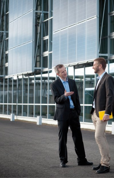 Geschäftsmänner vor Photovoltaik-Fassadenanlage (Bildquelle: REC)